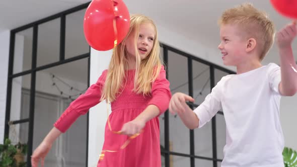 Little Boy and Girl Dancing with Red Heart Shape Balloons at Home