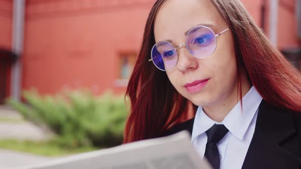 Thoughtful Young Woman Reading Newspaper on Street