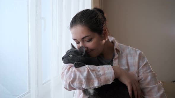 Young Brunette Woman with Cat Looks Out the Window