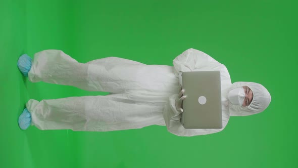 Man Wearing Uniform PPE, Medical Face Mask, Holding And Working With Laptop In Green Screen Studio