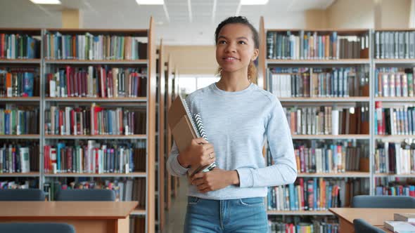 Cheerful Teenage Girl Walking with Books in High School Library Smiling