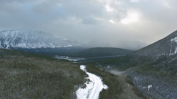 Aerial footage over a winter road and cloudy sky above the snowy forest in Alberta, Canada