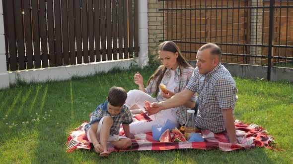 Happy Young Woman and Man Sit with Little Boy on Lawn