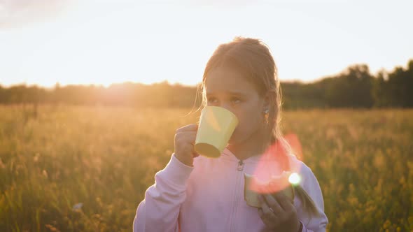 Cute Little Girl in the Field Eating a Bread and Drinking Milk at Sunset. Healthy Eating Concept.