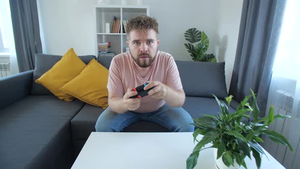 Attractive Man with Bristle and Toothy Grin Holding Joystick and Playing Videogames on Tv Sits at