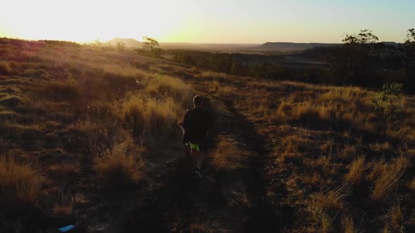 The camera follows a man as he walks towards a beautifully warm sunset with a scooter over his shoul