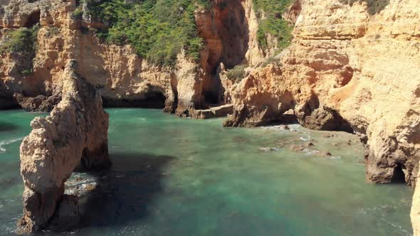 Rock formations in Rugged Algarve's southern cliffs encircled by emerald green sea, Portugal