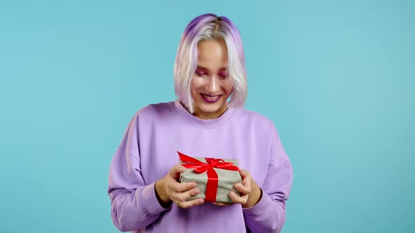 Cute Young Woman with Colorful Hair Holding Gift Box with Bow, She Wonders What Is Inside. Blue Wall