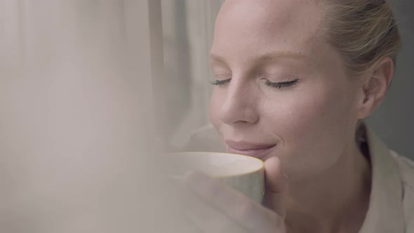 Blond woman with cup of tea at window