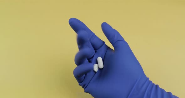 White Pills in Hand Dressed in Blue Medical Glove