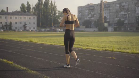 Back Angle View of Sportive Slim Woman Walking Along Athletic Field Doing Exercises. Wide Shot of