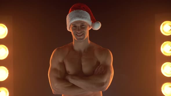 Portrait of Muscular Man Wearing Christmas Santa Hat Folded Hands on Smoky Background