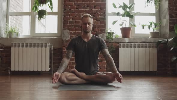 Handsome Man Doing Yoga in Lotus Pose in Studio with Wooden Floor and Windows.