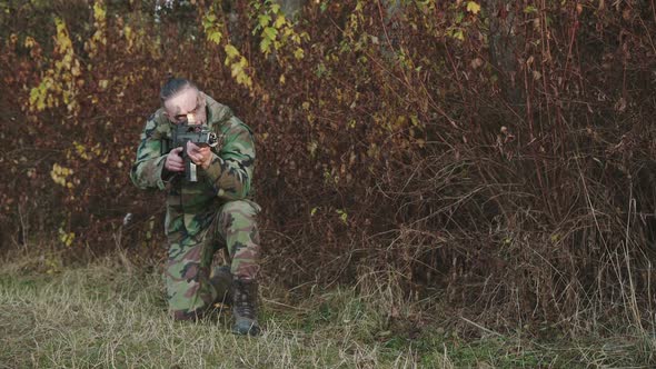The Hunter in Camouflage Aims a Gun at an Object in the Forest