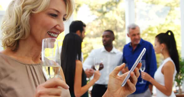 Smiling woman using mobile phone while friends interacting in background