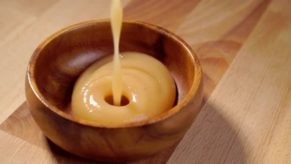 Pouring applesauce into a rustic wooden bowl in slow motion. Apple puree