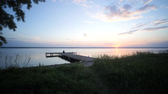 Lonely girl on wooden pontoon watching the sunset. Quiet place for meditation and prayer.