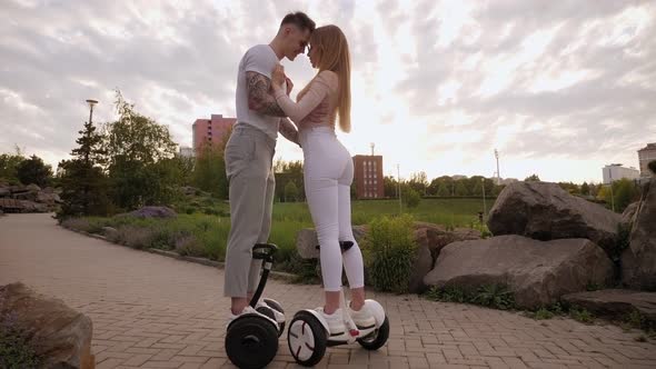 A Young Sports Couple Rides a Gyro Scooter and Kissed in a Beautiful Park