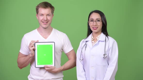 Young Asian Woman Doctor with Young Man Patient Showing Digital Tablet