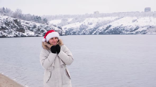 A Woman in Santa's Hat Walks Along the River in Nature in Winter Christmas Mood