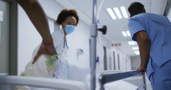 Diverse female and male doctors wearing face mask transporting patient