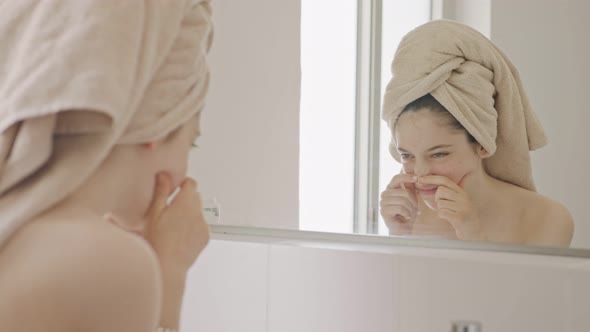 Teenage girl looking at the mirror in the bathroom - checking her face