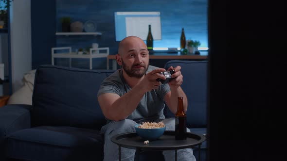 Excited Focused Man Sitting on Sofa Holding Joystick Playing Video Games