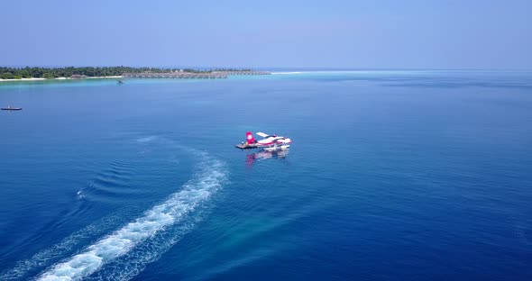Sea plane floating on blue lagoon near shore of tropical island with bungalows and resorts waiting f