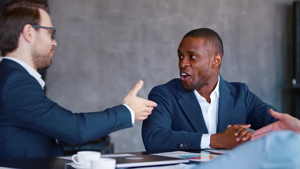 Smiling men in a suit shaking hands while sitting at office table