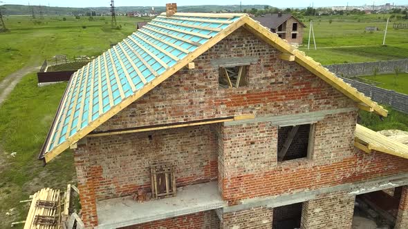 Aerial view of a brick house with wooden roof frame under construction.