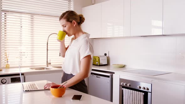 Woman using laptop while having coffee in kitchen