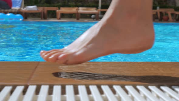 A Girl with Bare Feet Is Walking Along the Edge of a Pool of Blue Clear Water