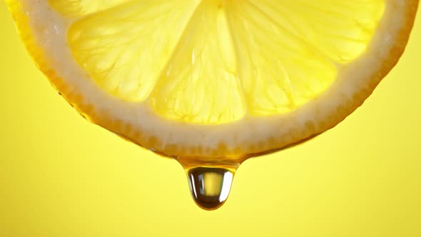 Super Slow Motion Macro Shot of Water Drop Falling From Lemon Slice on Yellow Background at 1000Fps