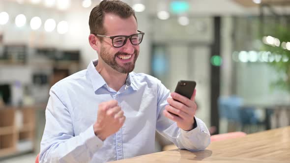 Businessman Celebrating Success on Smartphone in Office 