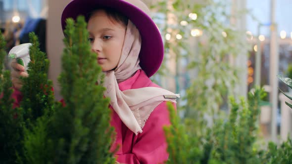 Cute Girl in Pink Hat Spraying Plants in Indoor Garden Orangery