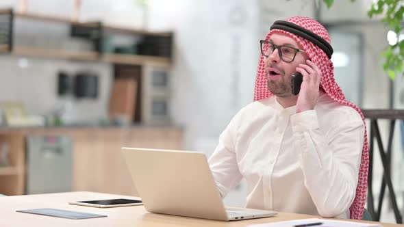Young Arab Businessman with Laptop Talking on Smartphone in Office
