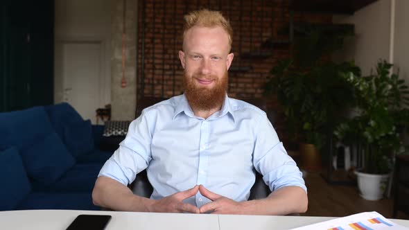 Smiling Redhaired Man Looks at the Camera and Waving Hand