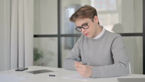 Young Man Writing on Paper in Modern Office