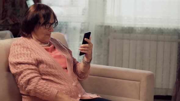 Grandmother In Glasses Scrolling On Screen On Cellphone. Mature Woman Holding Mobile Phone.