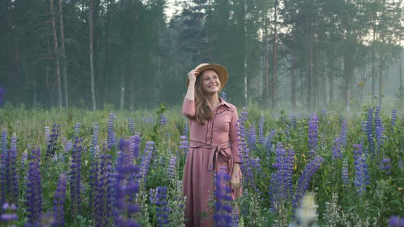 Blonde Woman Throws Away Hat Among Purple Lupin Flowers