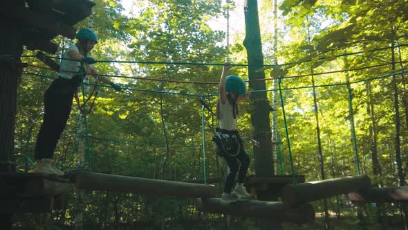 Young Woman and Her Daughter on an Attraction in the Park - the Girl Walking on the Logs Hanging on