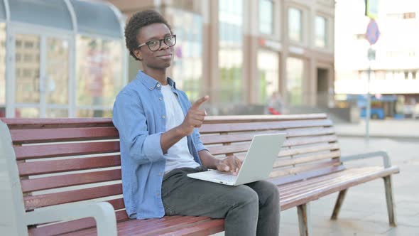 Young African Man Pointing at the Camera While Sitting on Bench Outdoor