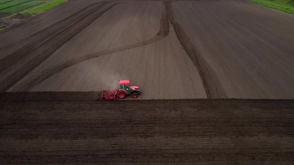 Aerial Shot of Tractor Plowing a Small Field with Blowing Dust in the Countryside of a Small Town