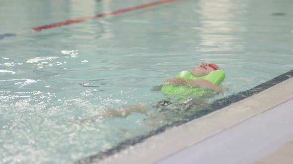 Caucasian Child Boy Kid Floating on Back in Swimming Pool Holding Green Board