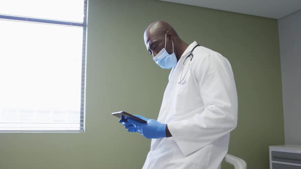 African american senior male doctor wearing face mask using digital tablet at hospital