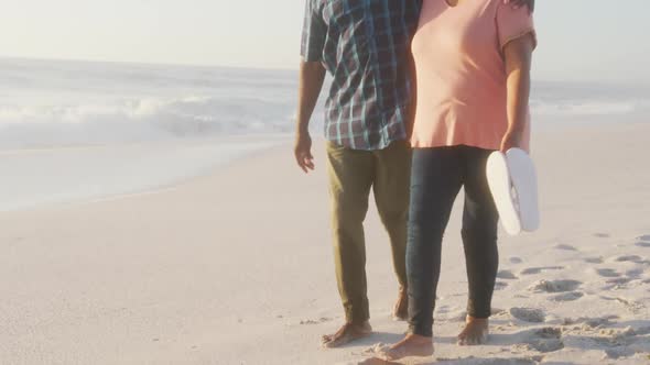 Smiling senior african american couple embracing and walking on sunny beach