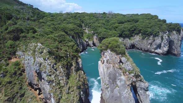 rocky coastline of Asturias Spain on sunny summer day flying between large boulders in ocean, aerial