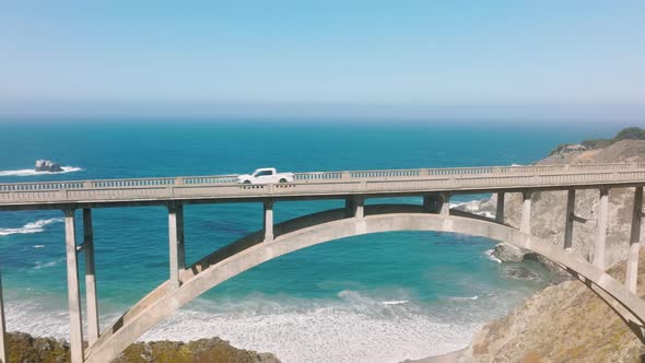 Cars Driving Along Scenic Arch Architecture Bridge with Blue Ocean Aerial View