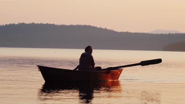 Man Sailing on River on the Boat Using Paddles - Orange Sunset