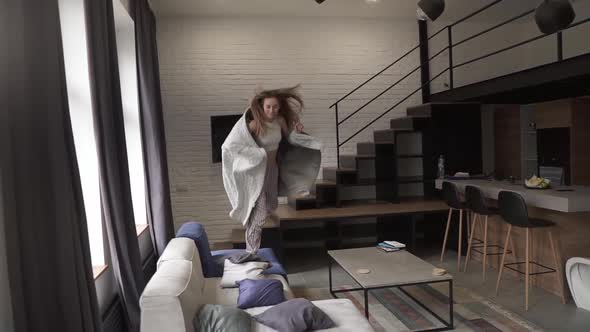 Relaxed Woman in Pajamas and Plaid Jumping on a Couch Running From the Stairs at Home